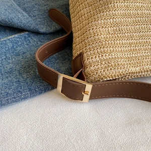 Detail of straw woven texture with brown leather strap and golden square metal buckle