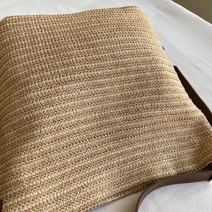 Close-up of fine straw weave texture and brown leather strap on a summer tote bag