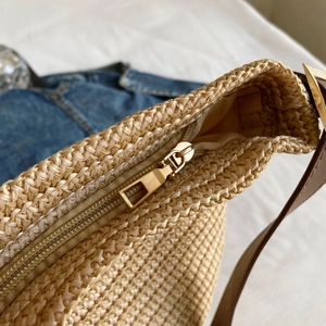 Detailed close-up of straw tote bag with gold metal zipper and brown leather strap