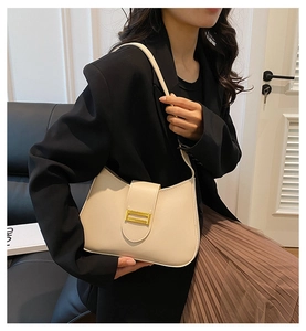 Detail view of a minimalist cream shoulder bag with a polished gold rectangular clasp