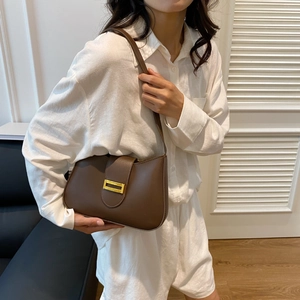 Detail of a brown leather shoulder bag featuring a gold rectangular decorative buckle