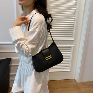 Close-up of black leather underarm bag with gold metal buckle worn on shoulder
