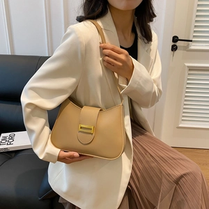 Close-up of khaki underarm bag with gold metal buckle on a model in white blazer