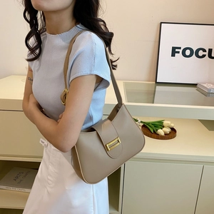 Close-up of khaki leather underarm bag with gold metal buckle on light blue knit sweater