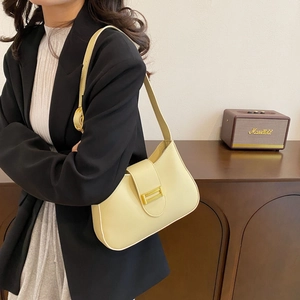 Detail of a minimalist cream shoulder bag with gold clasp worn with a black blazer