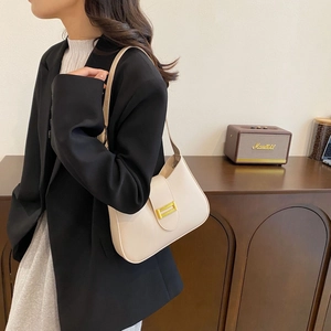 Detail of a beige crescent-shaped leather underarm bag with a gold buckle on model