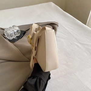 Detail view of cream white shoulder bag with golden round buckle and soft leather texture