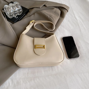 Detail of a creamy beige underarm bag with a gold metal buckle on a textured background