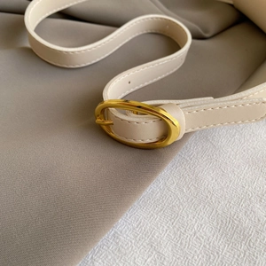 Detail of cream leather shoulder strap with polished gold oval buckle and fine stitching