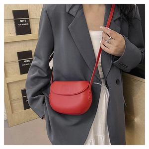 Red oval flap crossbody bag in matte leather worn by a model in a minimalist setting