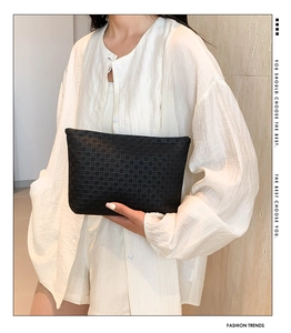 Close-up of black envelope clutch bag with geometric woven texture held by model