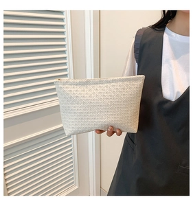 Detail of cream woven clutch bag with gold zipper and textured geometric pattern