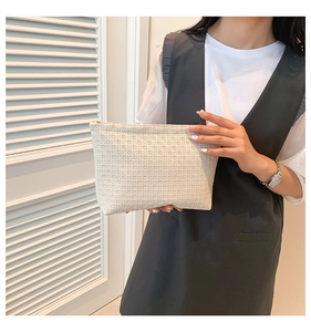 Close-up of minimalist beige woven clutch bag with textured pattern and metal zipper