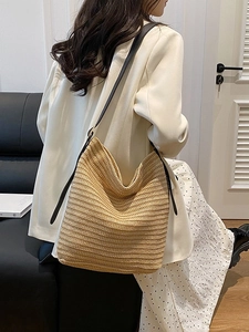 Minimalist straw tote bag with black leather straps shown on model in a modern room