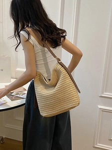 Minimalist straw shoulder bag with brown leather strap worn by model in chic interior