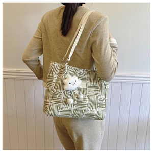 Detail of woven green and white canvas tote bag with a plush cloud charm accessory