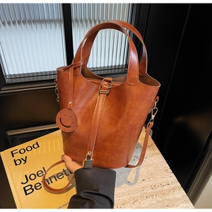 Détail d'un sac seau marron avec boucle en métal, poignée et charmant pendentif smiley