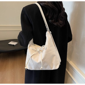 Detailansicht einer weißen Hobo-Tasche mit Schleife an einem Modell in schwarzem Mantel