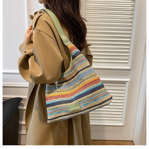 Detailed view of large striped woven shoulder bag with green leather strap on model