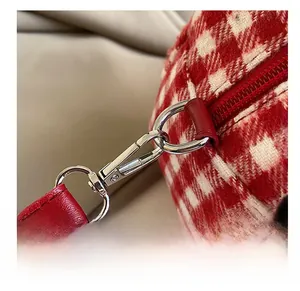 Detail of red leather shoulder strap attached to silver metal hook on plaid plush bag