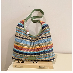 Close-up of bohemian woven straw tote bag with colorful stripes and green leather strap