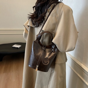 Sac seau marron foncé en cuir brillant avec cadenas doré et breloque sourire élégante