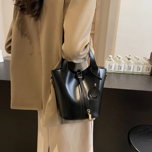 Sac seau tendance en cuir noir brillant avec détails dorés porté par un modèle