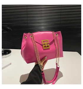 Detail of hot pink shoulder bag featuring a gold geometric lock and metal chain strap