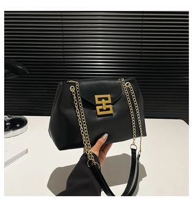 Close-up of black leather crossbody bag featuring a gold geometric buckle and chain