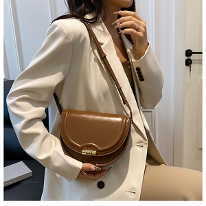 Dettaglio borsa a sella in pelle marrone con fibbia dorata abbinata a un blazer bianco