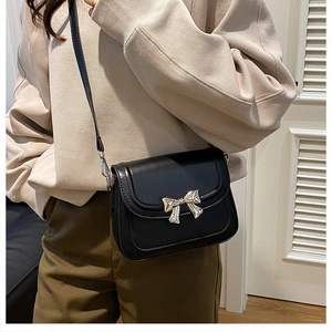 Détail d'un sac bandoulière noir en cuir avec boucle nœud dorée porté par un mannequin