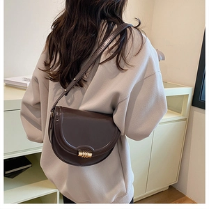 Dettaglio di una borsa a sella marrone scuro in pelle lucida con fibbia dorata chic