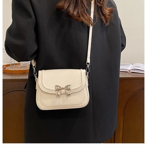 Detailansicht der cremefarbenen Umhängetasche mit eleganter Metallschleife auf dunklem Anzug