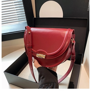 Dettaglio di una borsa a sella rosso scuro con chiusura dorata in scatola regalo