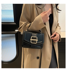 Detail of a black leather crossbody bag featuring a large gold rectangular metal buckle