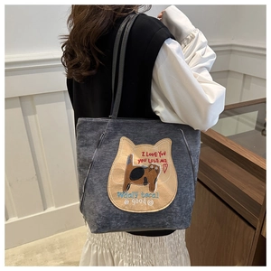 Detail of gray canvas tote bag featuring cat embroidery and decorative side zippers