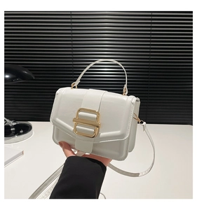 Close-up of white leather handbag featuring a bold gold metal buckle and hand-held pose
