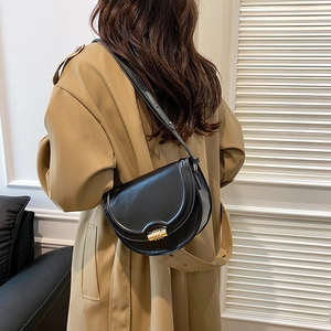 Borsa a sella classica in pelle nera con chiusura dorata su un trench coat beige