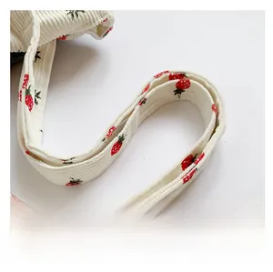 Detail of white corduroy shoulder strap featuring cute red strawberry prints and textures