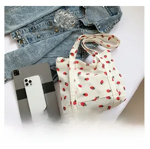 Detail of white corduroy tote bag with strawberry prints showing capacity next to a tablet