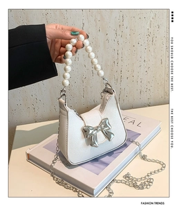 Detail of white pearlescent mini bag with silver bow and pearl handle on a magazine
