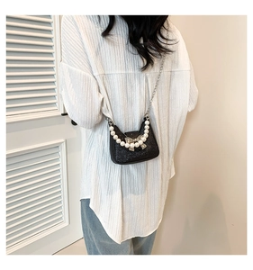 Detail of black glitter crossbody bag with pearl handle and silver bow on white shirt