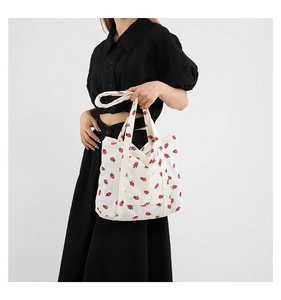 On-shoulder view of corduroy tote bag with red strawberry print and long strap