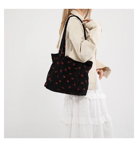 Detailed texture of black corduroy tote bag with embroidered red strawberry patterns