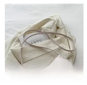 Detail of light beige saddle bag with round buckle on white blazer and artsy book