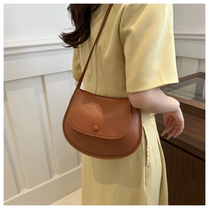 Detail of a brown saddle bag with elegant clasp and slim shoulder strap on model