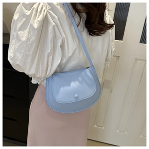 Detail of light blue crescent saddle bag worn by a model in a minimalist home setting