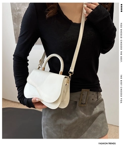 Detailed view of a white saddle bag with a woven handle and gold magnetic closure
