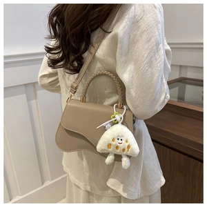 Detail of beige saddle bag featuring a woven handle and cute cheese plush pendant