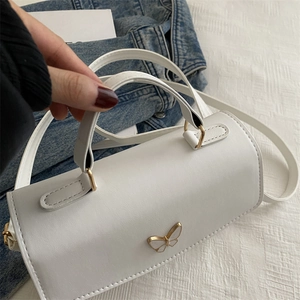 Close-up of white cylindrical crossbody bag with gold butterfly accent on soft texture